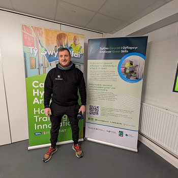 man standing in front of ty gwyrddfai posters